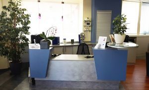 Moderner Empfangsbereich in einem Büro mit Schreibtisch, Pflanzen und Informationsmaterial.